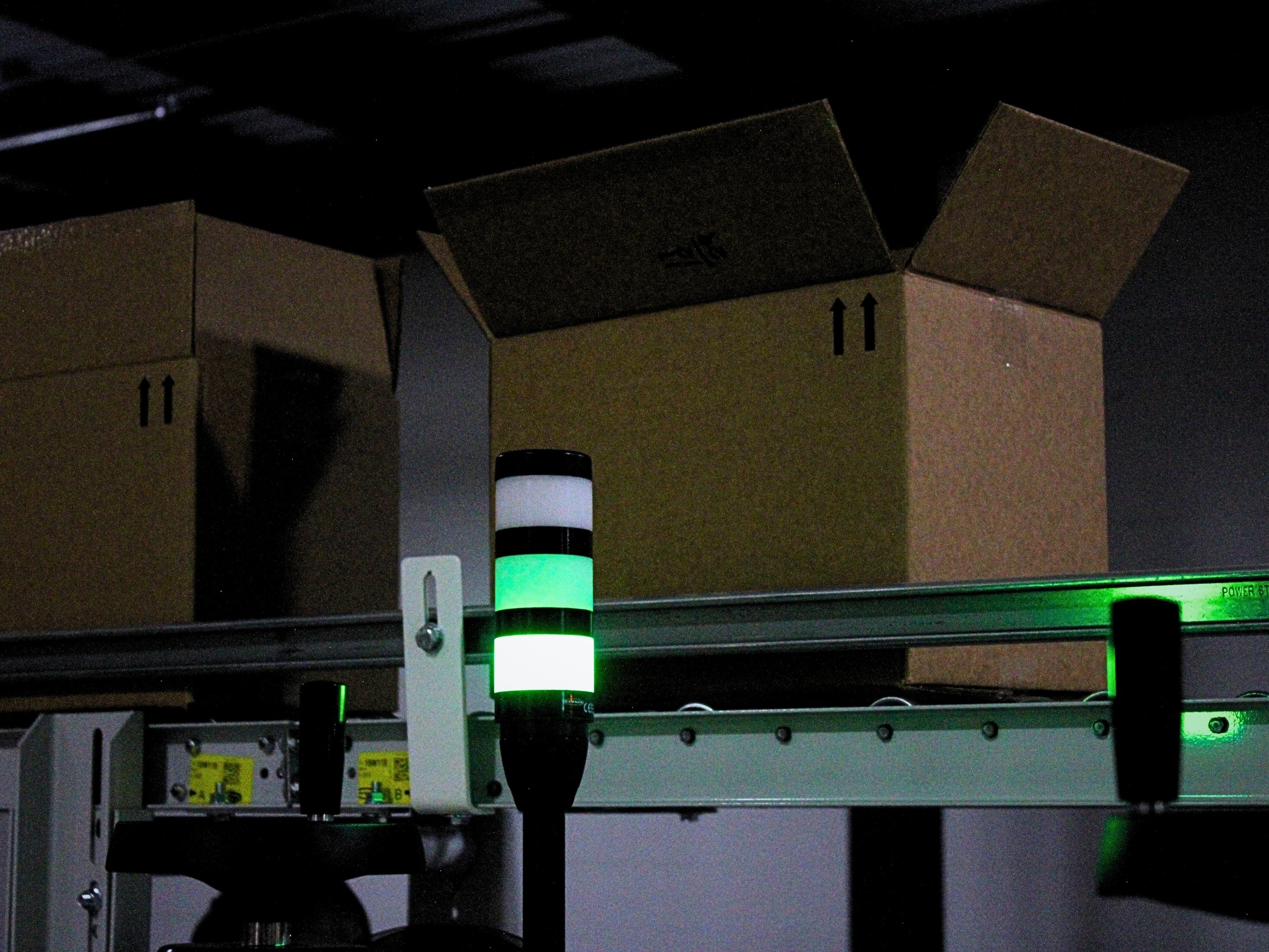 Cartons on an overhead conveyor beside a green status light