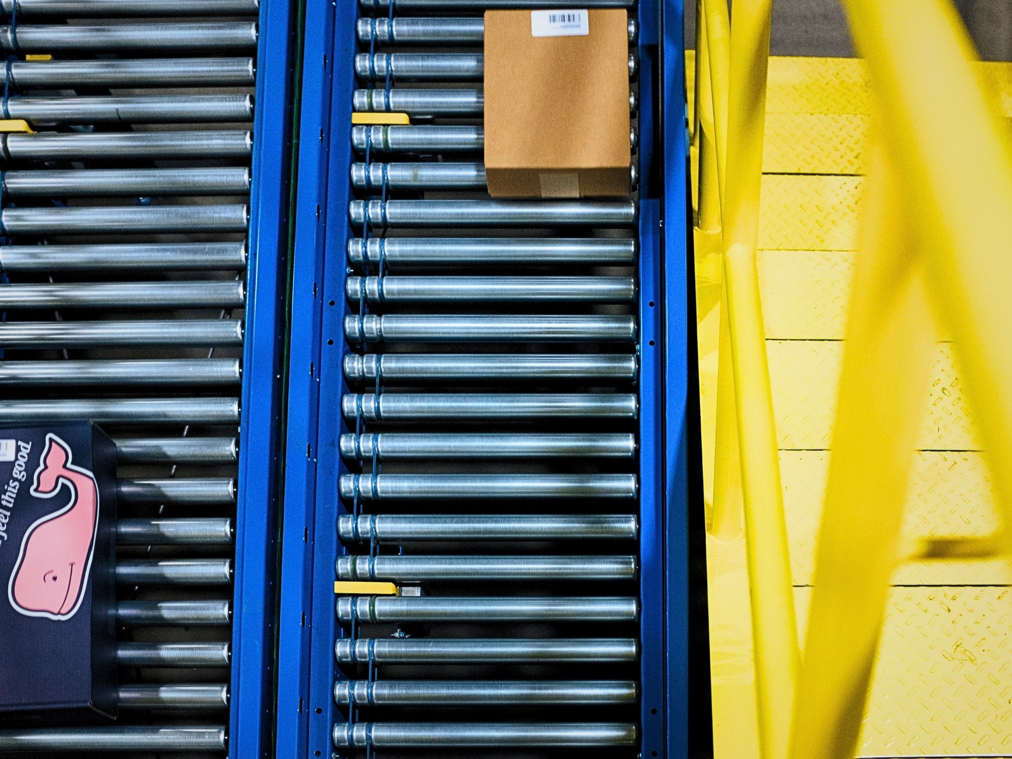 Overhead view of cartons on parallel roller conveyor lanes beside a yellow access platform
