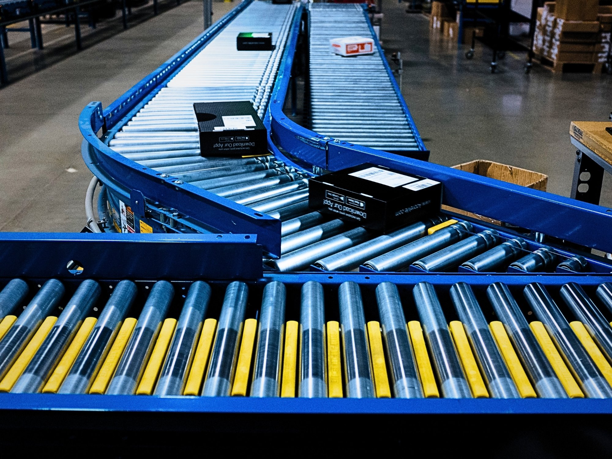 Black cartons following a curved roller conveyor toward an adjoining conveyor section