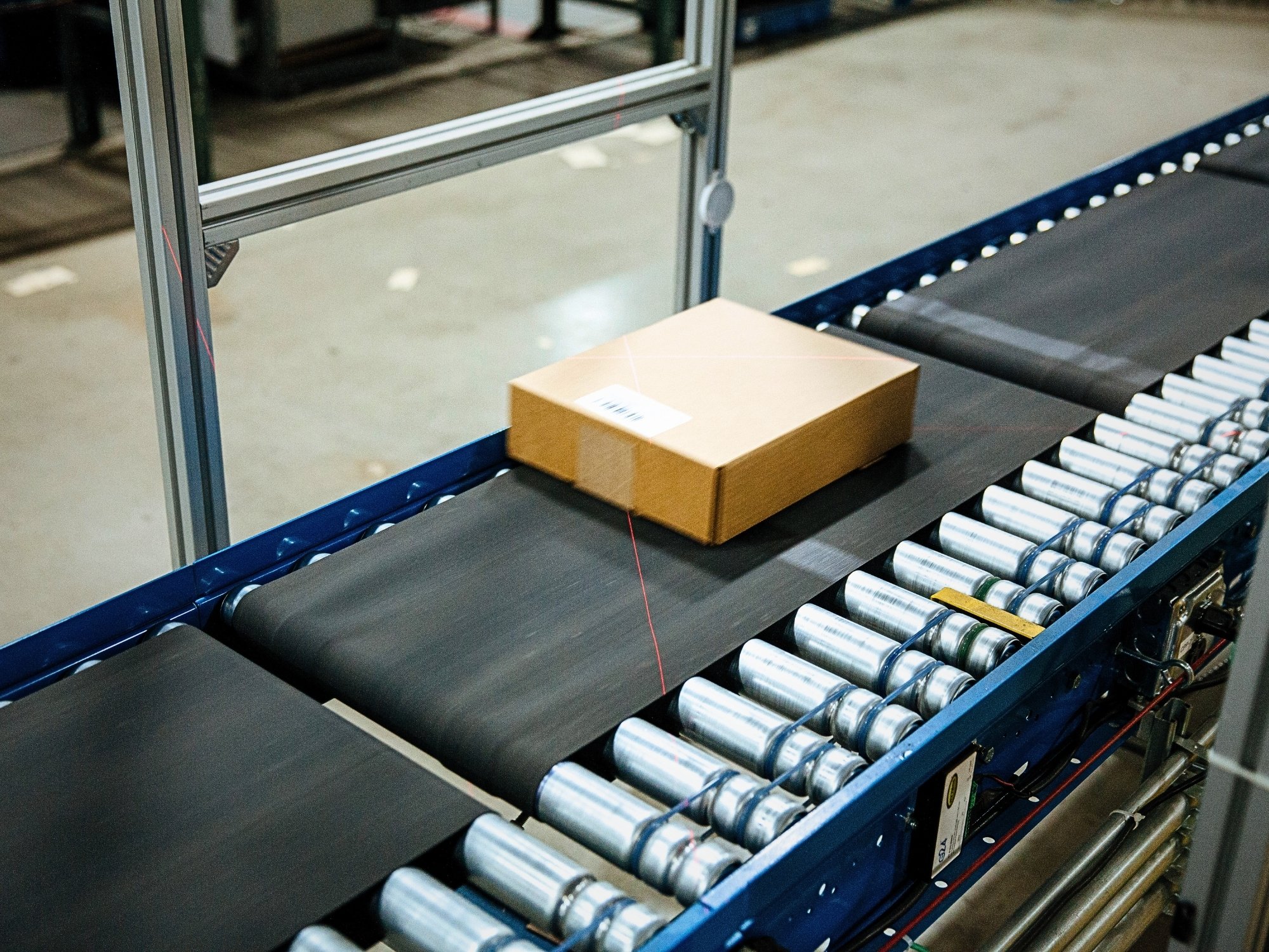 Shipping carton on a belt conveyor section between roller conveyors.