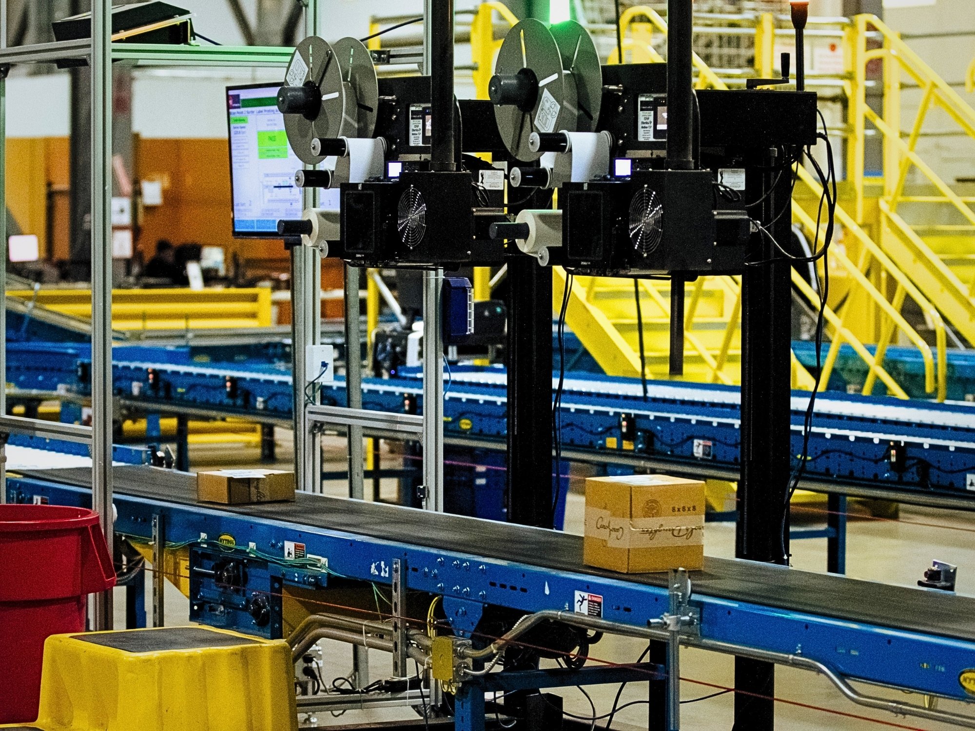 Overhead label-printing and application equipment positioned above a carton conveyor