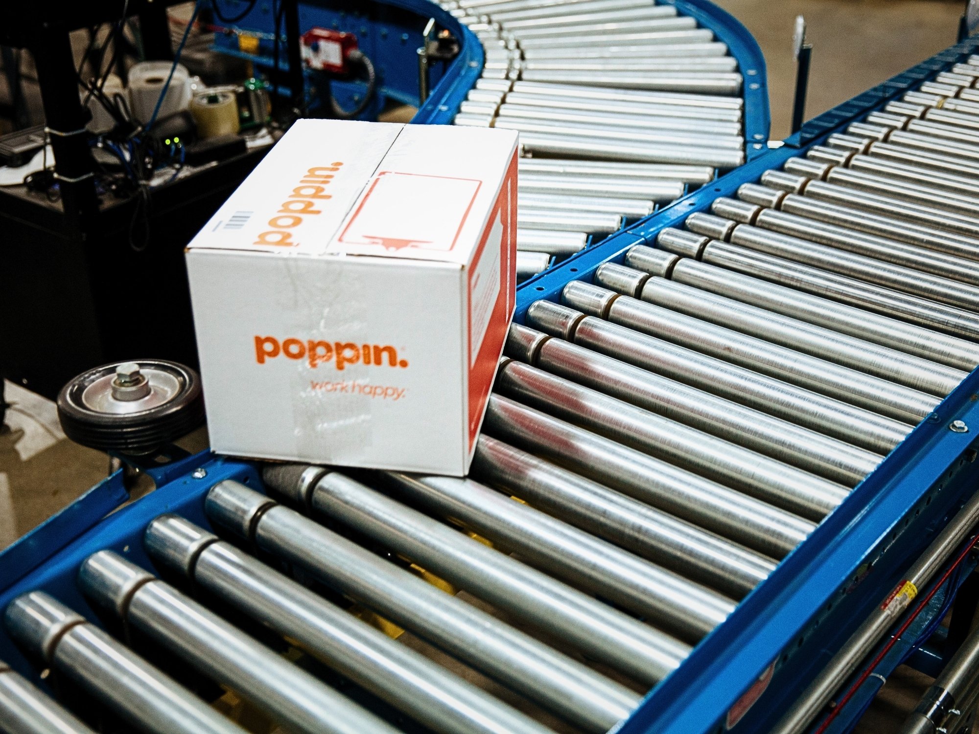 Branded shipping carton passing guide wheels at a roller conveyor junction