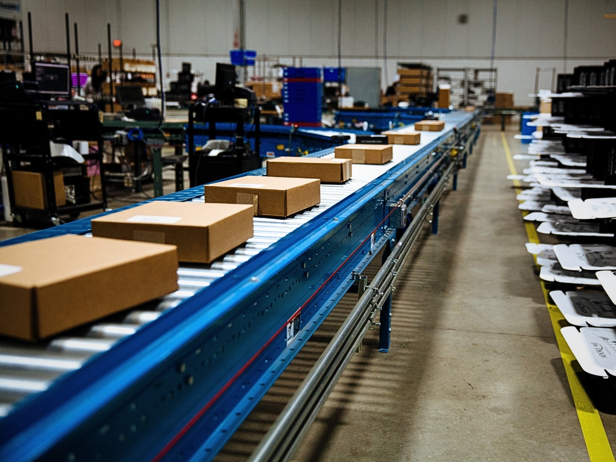 Shipping cartons spaced along a takeaway conveyor beside fulfillment workstations