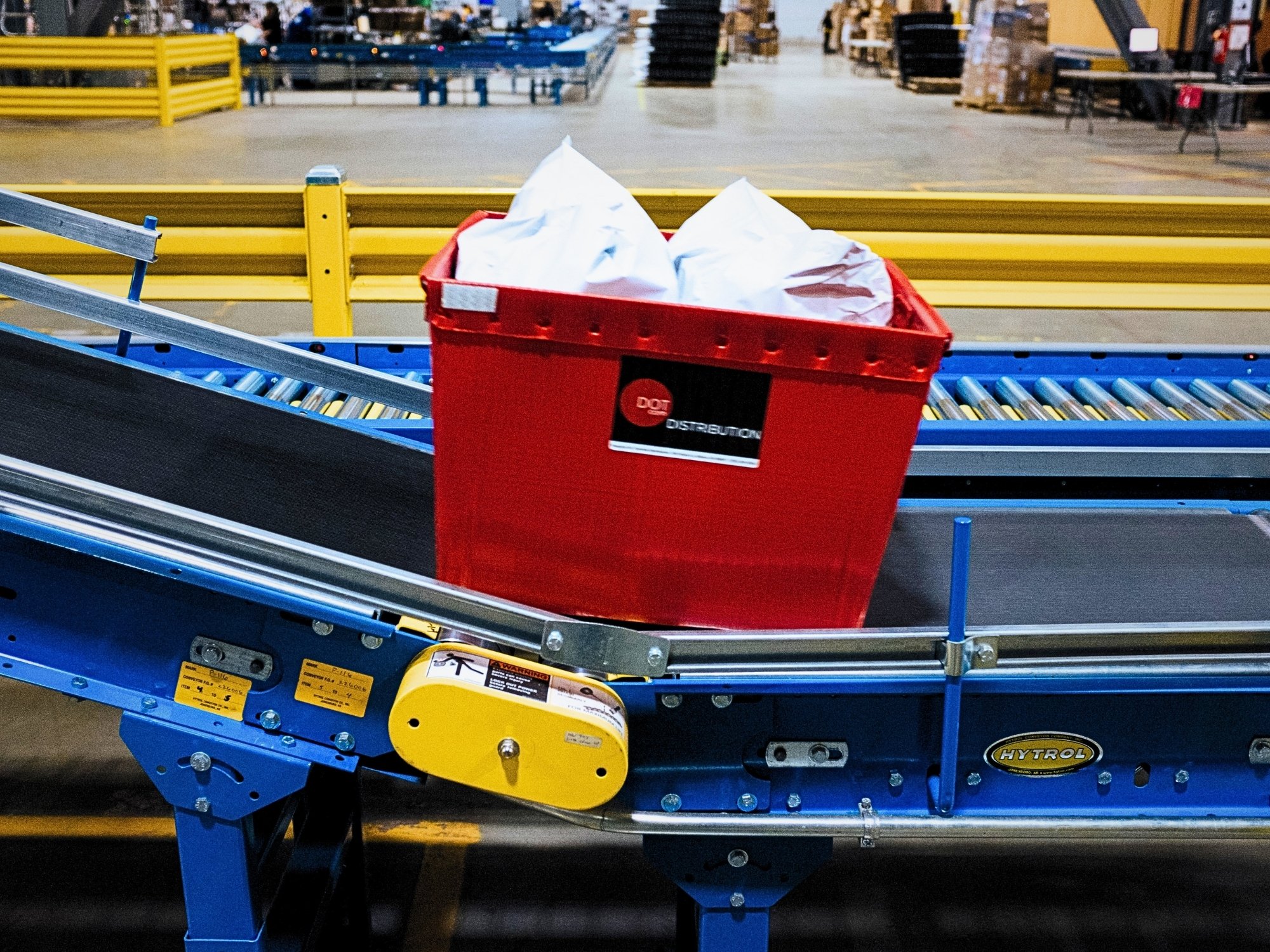 Red tote carrying product on a belt conveyor alongside the carton-handling lanes.
